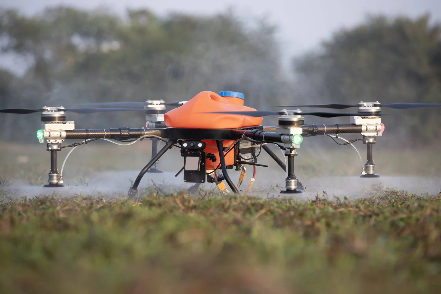 Orange agricultural drone spraying above the ground